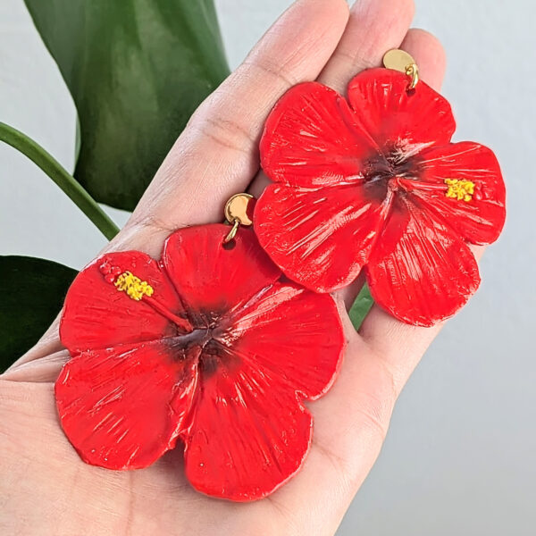red hibiscus earrings on palm of hand